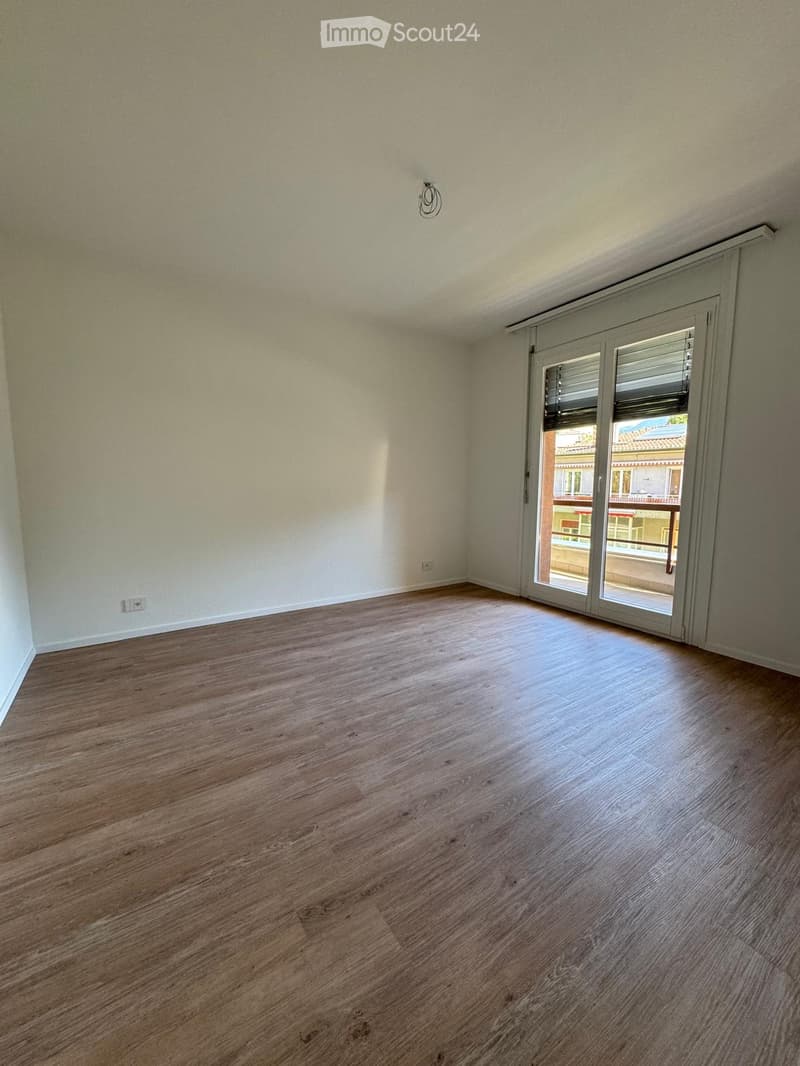 Empty room with wooden flooring, white walls, and a large sliding glass door leading to a balcony.