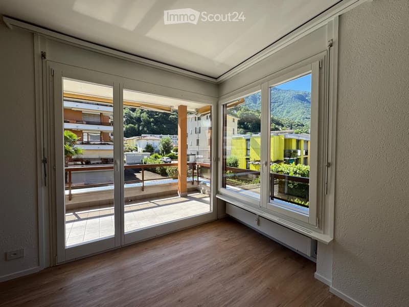 Empty room with wooden flooring, large windows, and sliding glass doors leading to a balcony with a scenic mountain view.