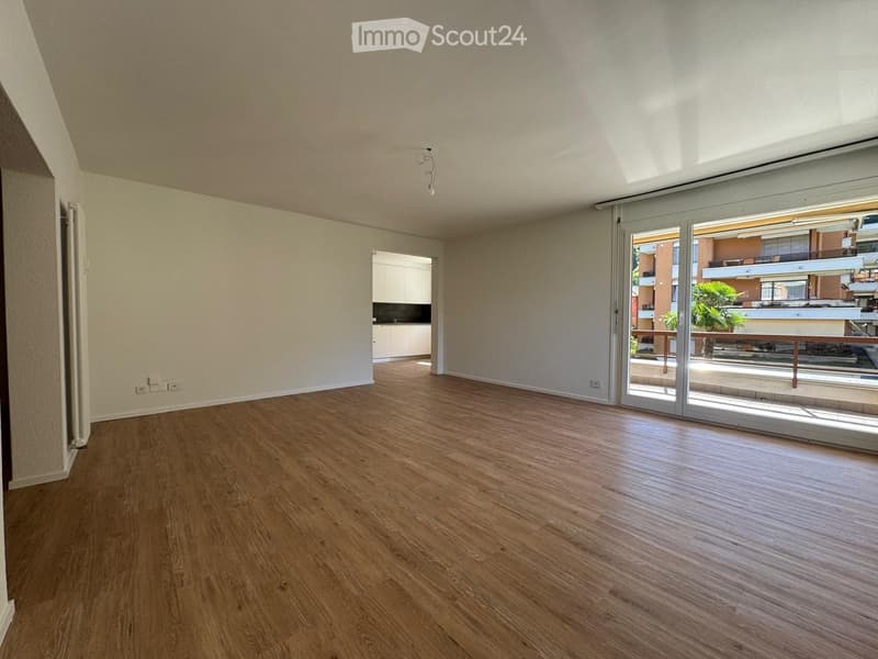 Empty room with wooden flooring, white walls, and large sliding glass doors leading to a balcony area.