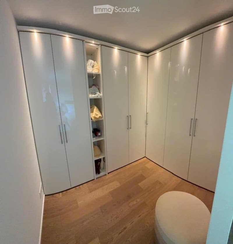 walk-in closet with white cabinets, wooden floor, white ottoman