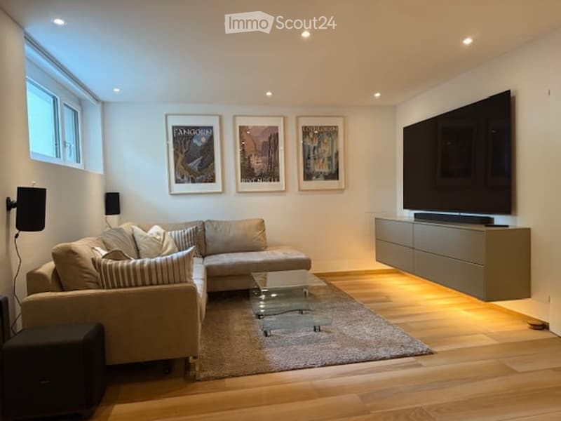 open-plan living/dining area, modern design, beige sectional sofa, glass center table, large TV on wall, hardwood floors, speakers