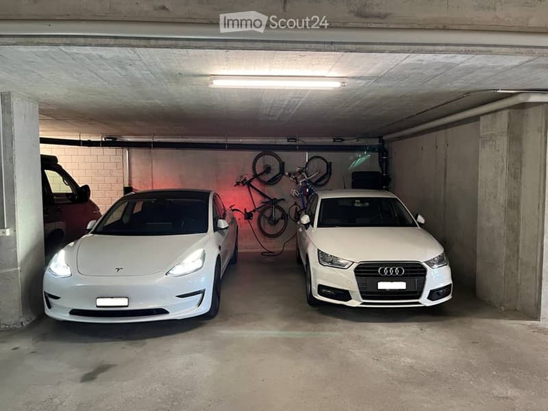 underground parking garage, two cars parked, bicycles mounted on wall, charging station