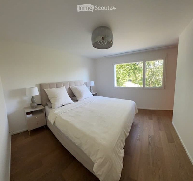 Large white double bed, wooden floors, white walls, two bedside tables with lamps, large window