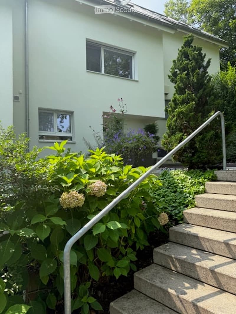 white painted house, raised ground floor, stairs leading to entrance, garden with shrubs and flowers