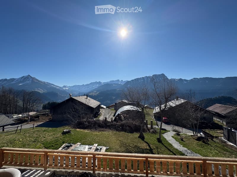 Balcony overlooking a scenic mountain landscape with several houses and a winding road below.