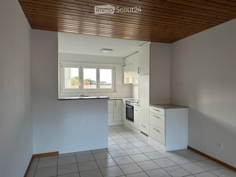 Modern kitchen with white cabinets, a built-in oven, a sink, and a central island counter. The space features tiled flooring and a wooden ceiling.
