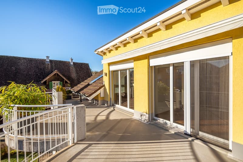 Balcony with glass sliding doors, metal railing, and a view of neighboring houses with tiled roofs.