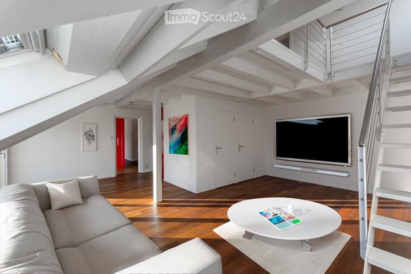 Modern living room with exposed wooden beams, white walls, hardwood flooring, a grey sectional sofa, a white coffee table, a large flat-screen TV, and artwork on the walls.