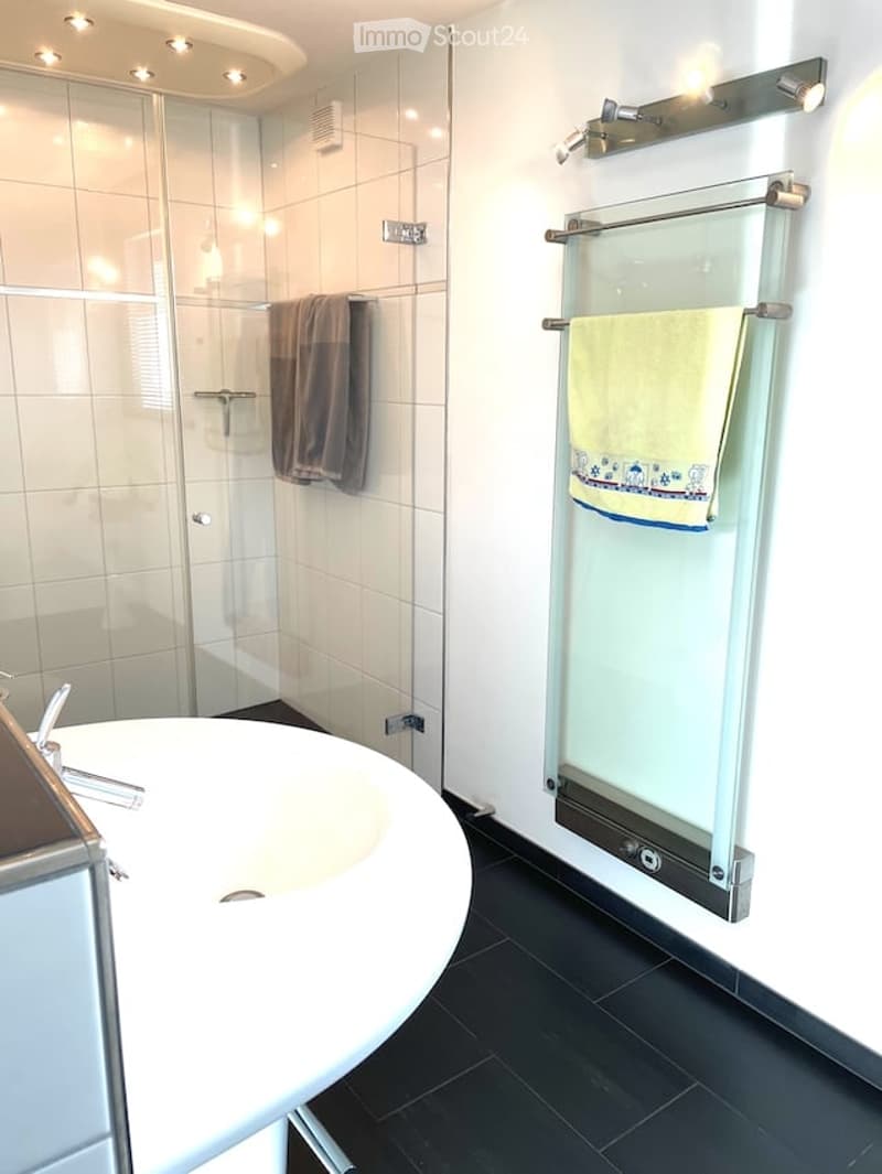 Modern bathroom with a white sink, glass-enclosed shower, and towel rack with towels.
