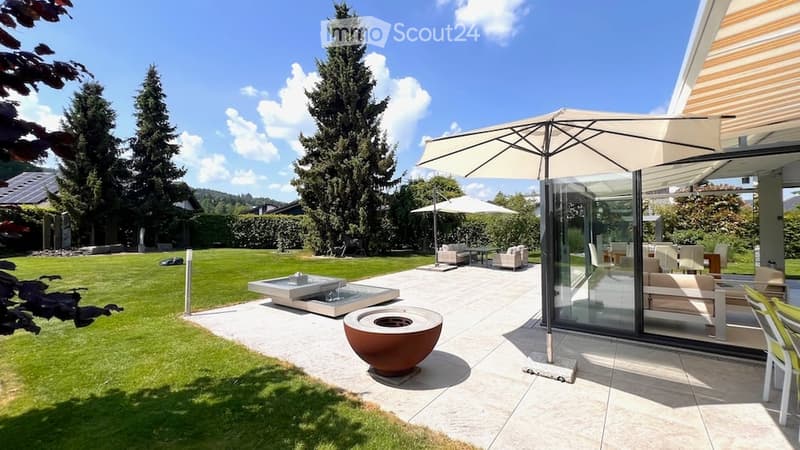 Well-maintained garden with a patio area, outdoor seating, umbrella, fire pit, and water feature.