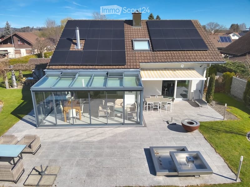 Modern house with a spacious patio area, featuring a glass-enclosed dining area, outdoor seating, a small pool, and a fire pit.