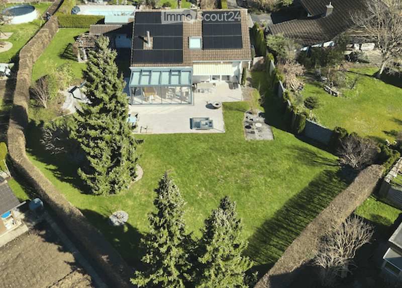 Aerial view of a well-maintained garden with a swimming pool, patio area, and solar panels on the roof of the house.