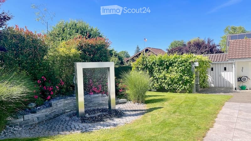 Well-maintained garden with a modern water fountain, lush greenery, and a neatly trimmed lawn.