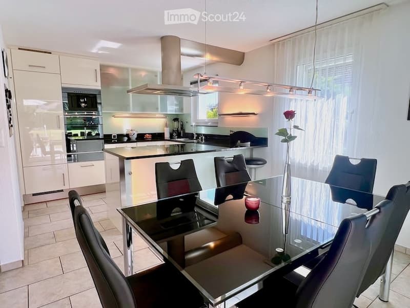Modern kitchen with white cabinets, stainless steel appliances, a central island, and a dining area with a glass table and black chairs.