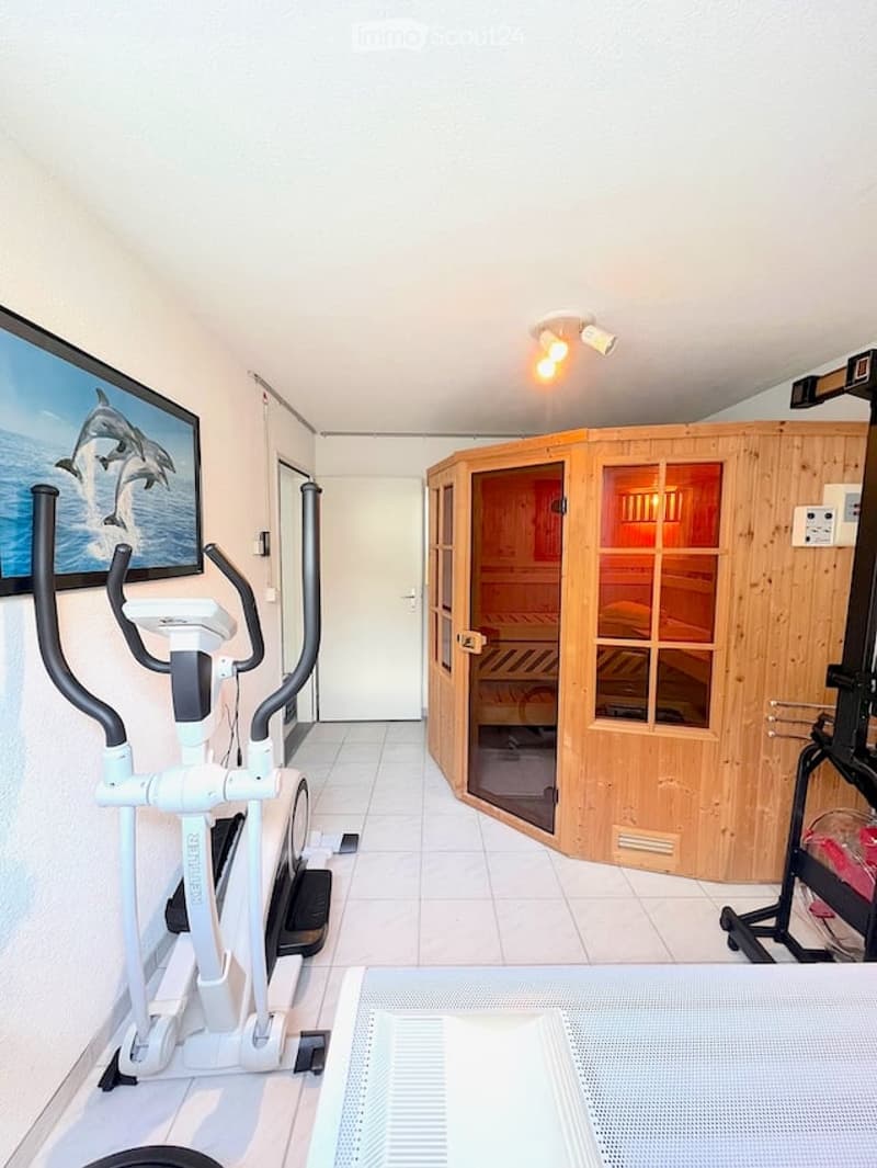 Well-lit room with a sauna, exercise bike, and a picture frame on the wall.