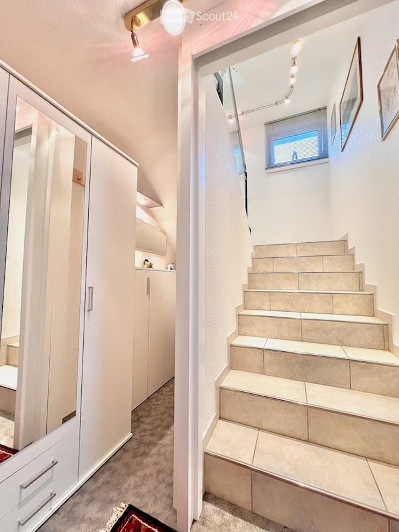 A modern hallway with a staircase leading upwards, white built-in wardrobes, and a small window at the top of the stairs.