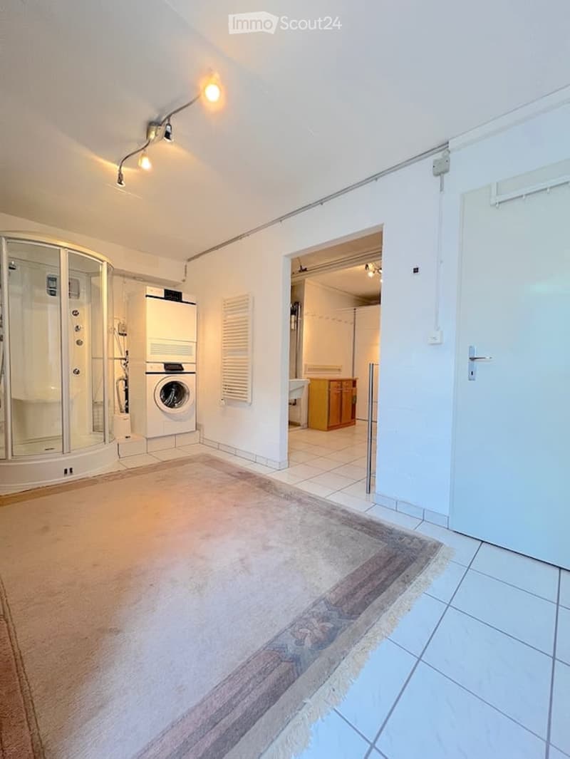 Modern bathroom with a glass-enclosed shower stall, a private washing machine, a radiator, and a small cabinet. The space is bright with white walls and tiled flooring.
