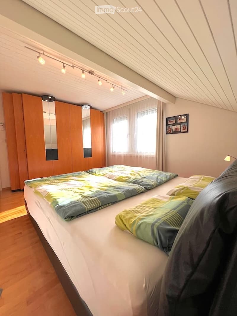 Modern bedroom with a double bed, wooden wardrobe, large window with curtains, and picture frame on the wall.
