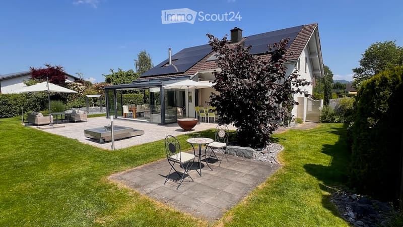 Well-maintained garden with a patio area, outdoor seating, and a covered dining area connected to the house.