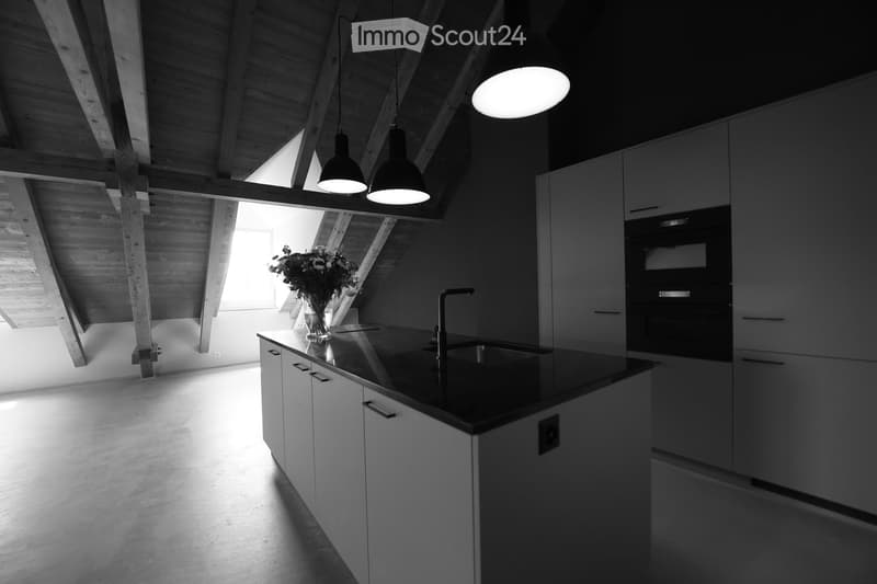 Modern kitchen with white cabinets, black countertop, stainless steel sink, and pendant lights. A vase with flowers is placed on the counter.