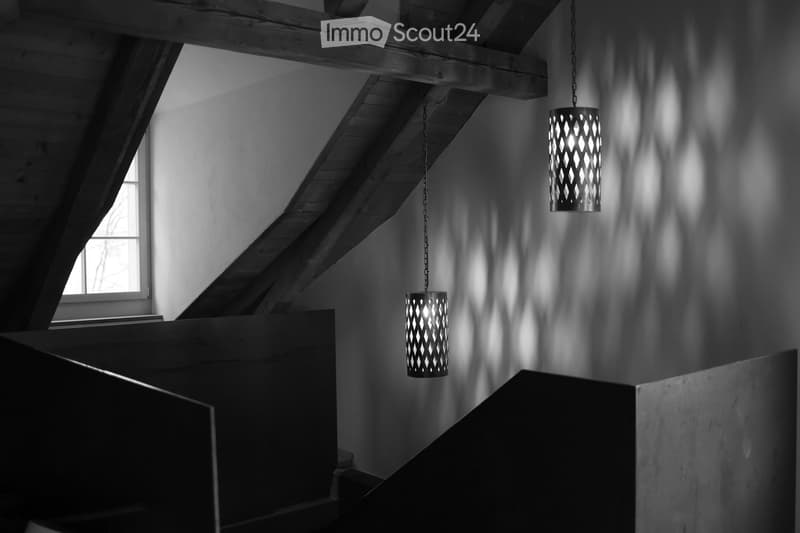 Staircase with exposed wooden beams and geometric patterned pendant lights casting shadows on the walls.