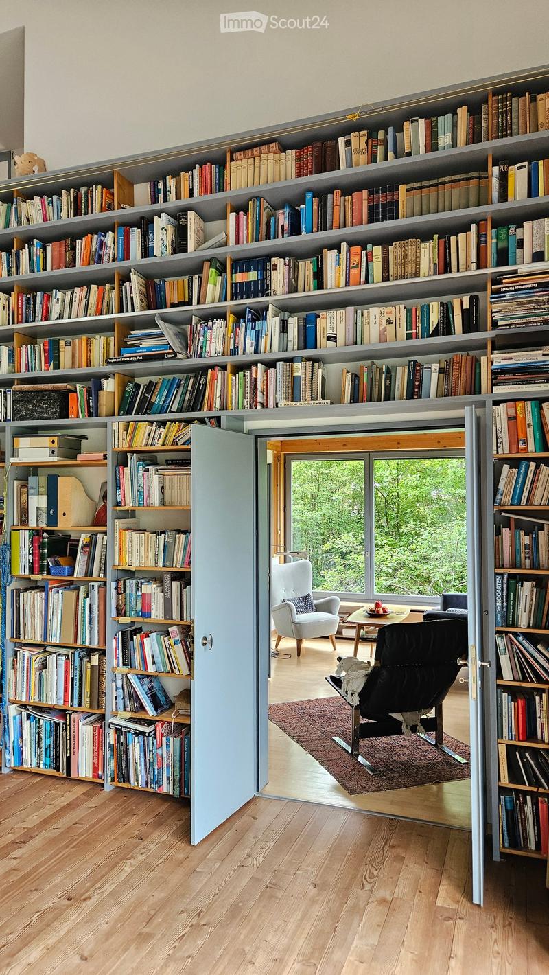 Furnished Room. A room with tall, built-in bookshelves filled with books, a light blue cabinet door, a small seating area with a white armchair, a black leather chair, a small table, and a patterned rug.