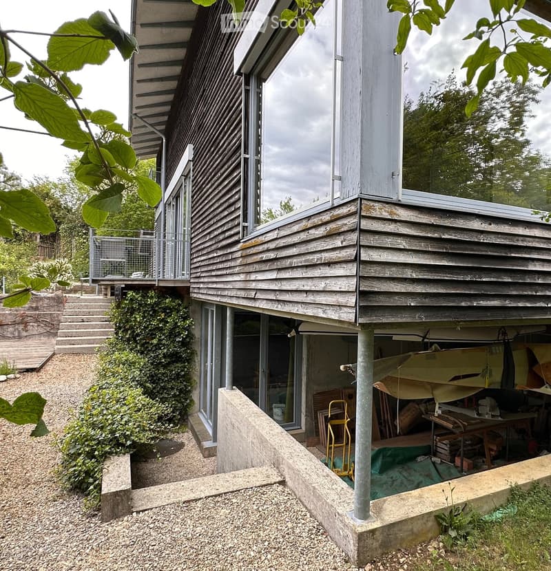 Building. Modern two-story wooden house with large windows, raised ground floor, and a covered garage area.