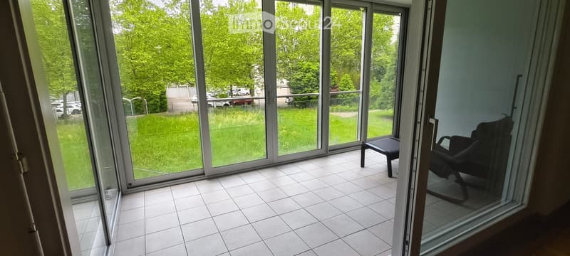 Balcony with tiled floor, large glass sliding doors, and a single black chair.