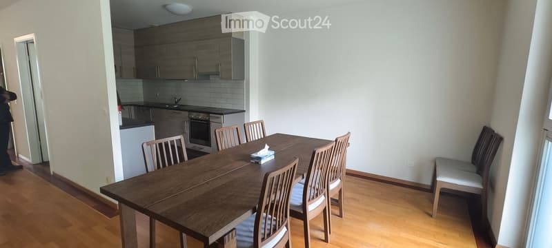 Dining area with a wooden dining table and chairs, a bench with cushions, and an adjacent kitchen area with cabinets, an oven, and a sink.