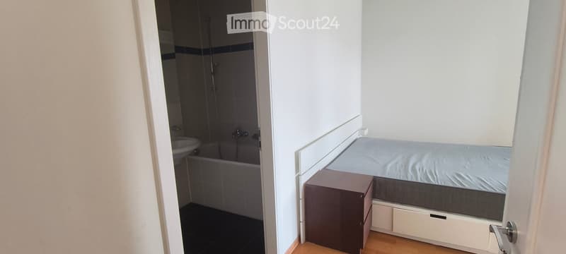 A compact bedroom with a single bed, nightstand, and an adjacent bathroom featuring a bathtub and sink.