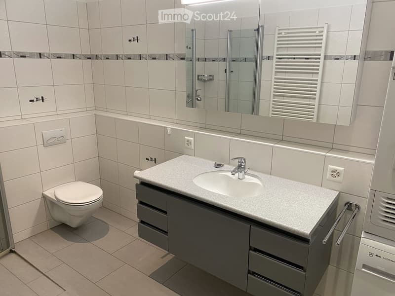 modern bathroom with white tiles, white toilet, white sink, mirror, towel rack, shower enclosure