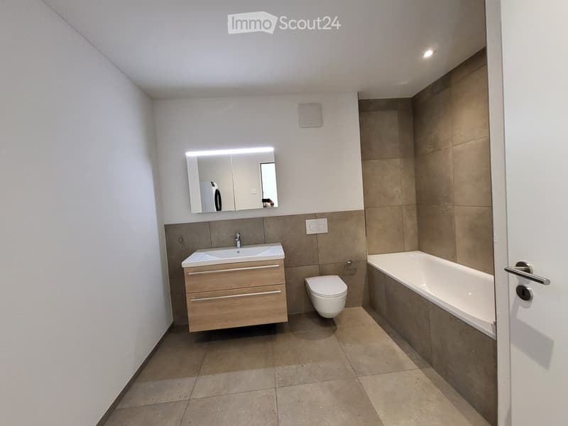 Modern bathroom with a double sink, mirror, toilet, bathtub, and wooden cabinet.
