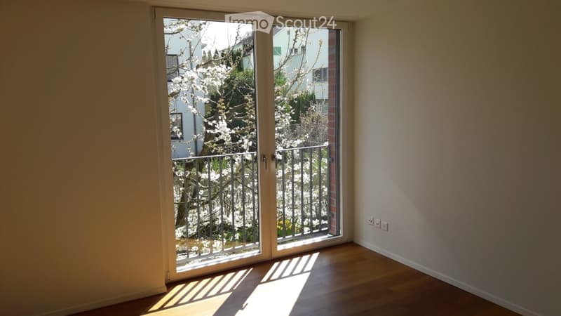 Empty room with wooden flooring, large sliding glass doors leading to a balcony, and white walls.
