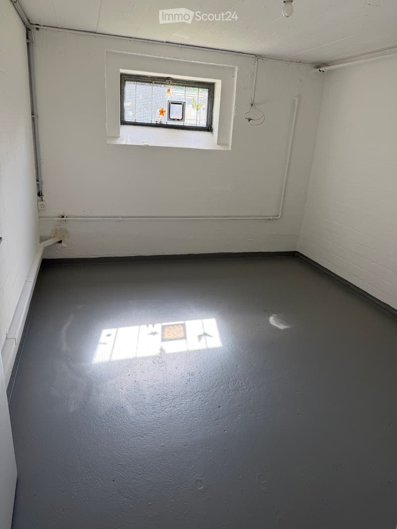 Empty room with white brick walls, grey concrete floor, and a small window with a decorative glass design.