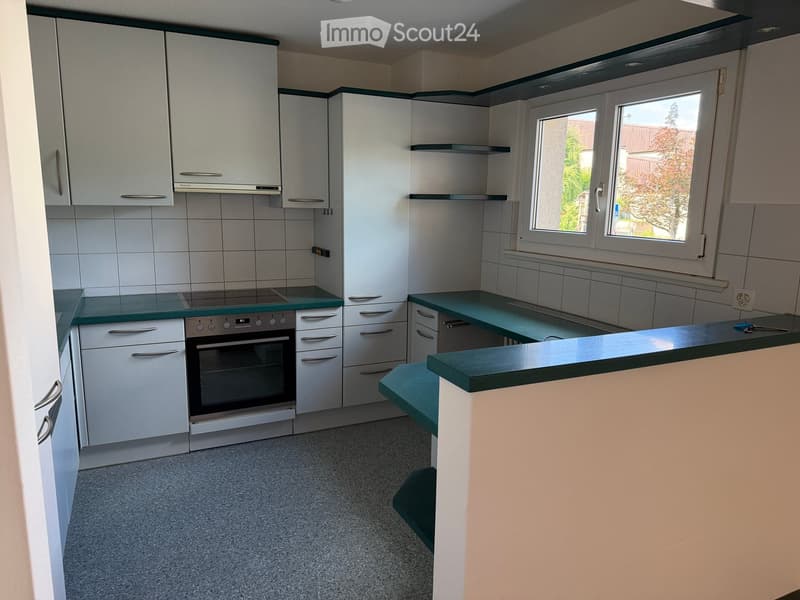 Modern kitchen with white cabinets, green countertop, and built-in oven. Features large windows and a clean, organized layout.