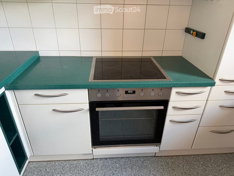 Modern kitchen with white cabinets, green countertop, induction cooktop, and built-in oven.