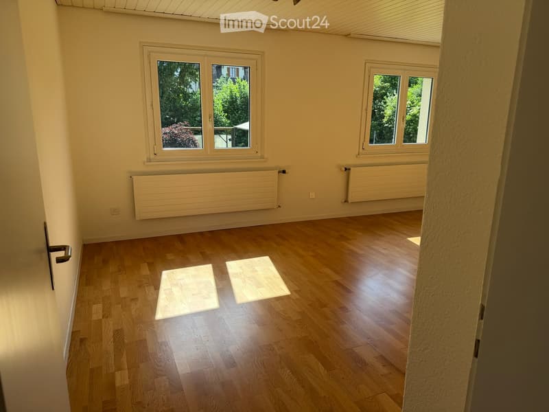 Empty room with wooden flooring, white walls, two windows, radiators, and a door.