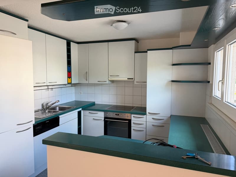 Modern kitchen with white cabinets, green countertops, stainless steel sink, oven, and dishwasher. Features a window and built-in lighting.