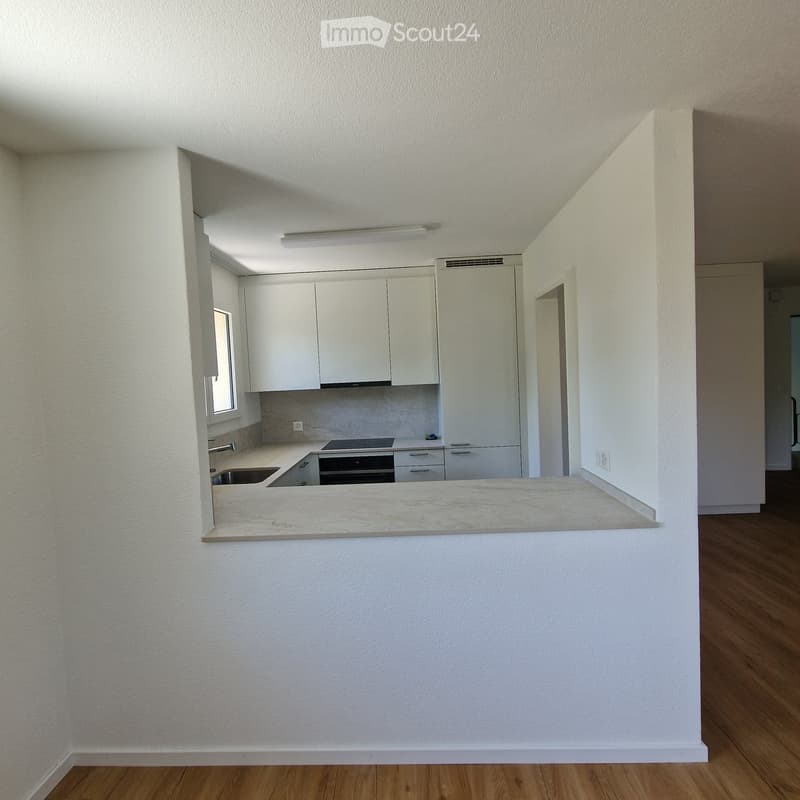 Modern kitchen with white cabinets, a marble countertop, a sink, and an oven. The space is open to a wooden-floored living area.