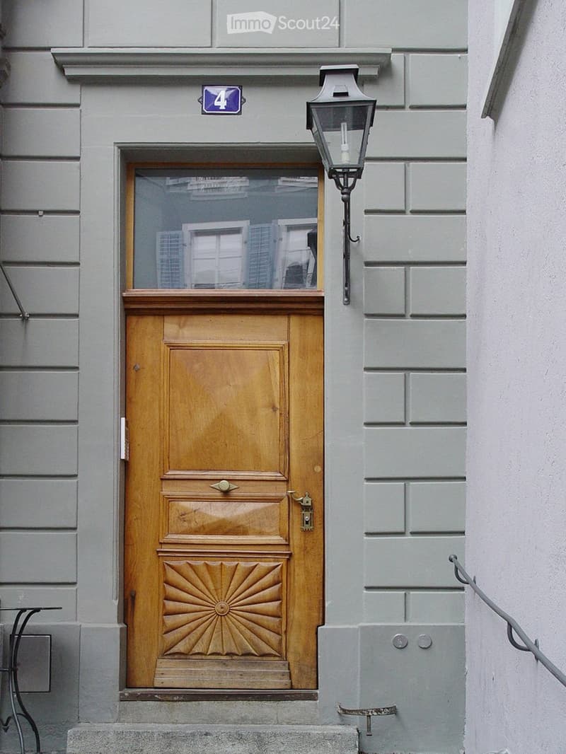 Wooden front door with decorative panels, glass window above, and a lantern-style light fixture mounted on the wall.