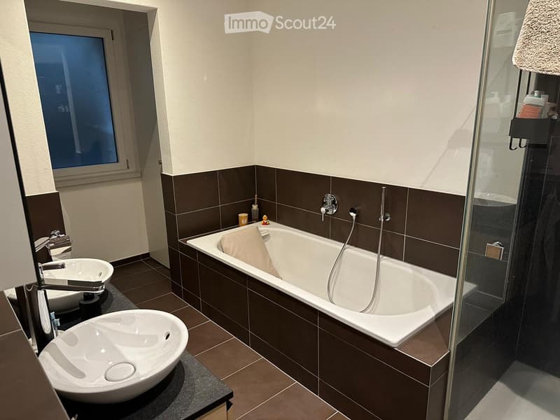 Modern bathroom with a bathtub, two sinks, a shower, and a towel on the edge of the tub.