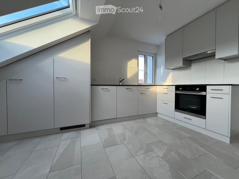 Modern kitchen with white cabinets, stainless steel oven, and grey tiled floor. Features a skylight and large windows for natural light.