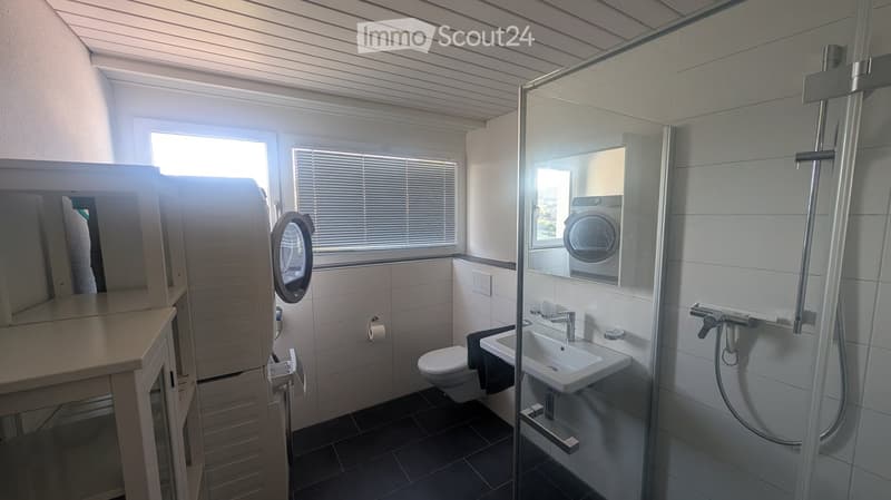 Modern bathroom with a glass-enclosed shower, a sink with a faucet, a toilet, a mirror, and a cabinet. The room features white tiled walls and a dark tiled floor.