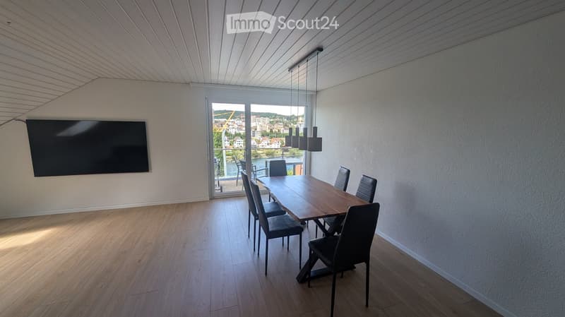 Modern dining room with wooden floor, large window offering a scenic view, dining table with chairs, and a flat-screen TV mounted on the wall.
