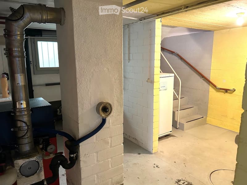 Empty basement space with exposed brick walls, concrete floor, metal staircase, and various utility equipment including a water heater and boiler.