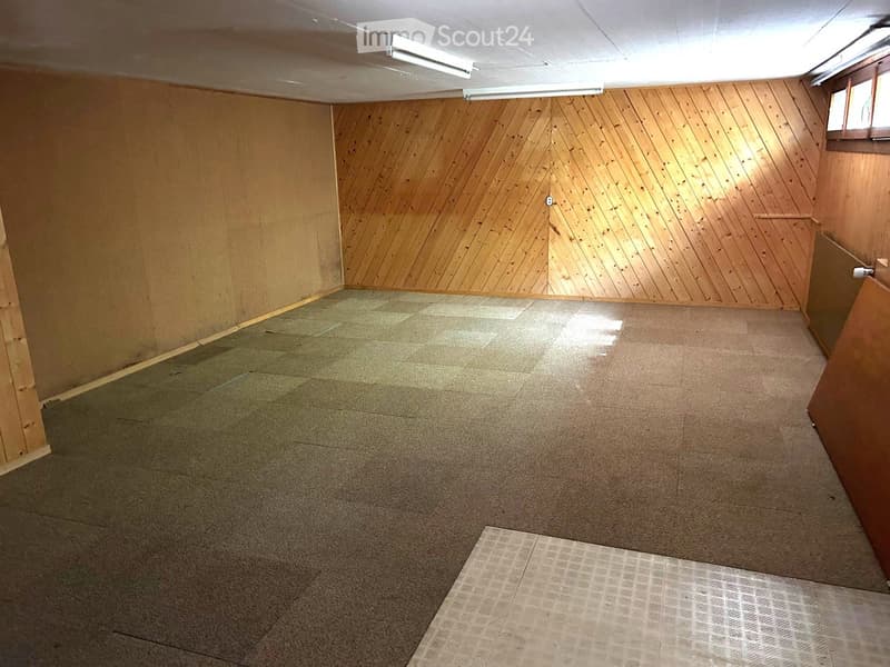 Empty room with wooden panel walls, carpeted floor, and fluorescent lighting. No furniture or equipment present.