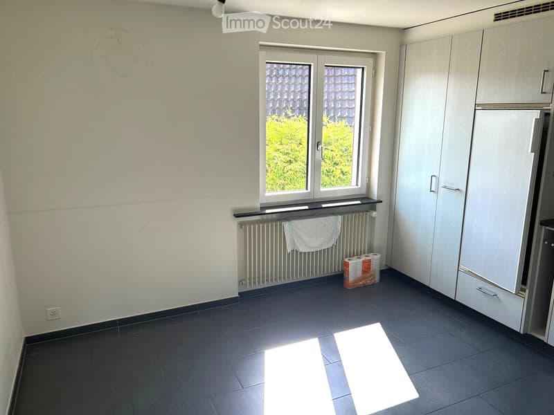 Empty room with dark tiled floor, white walls, a window with a view of greenery, a radiator with a towel, and a stack of paper towels on the floor.