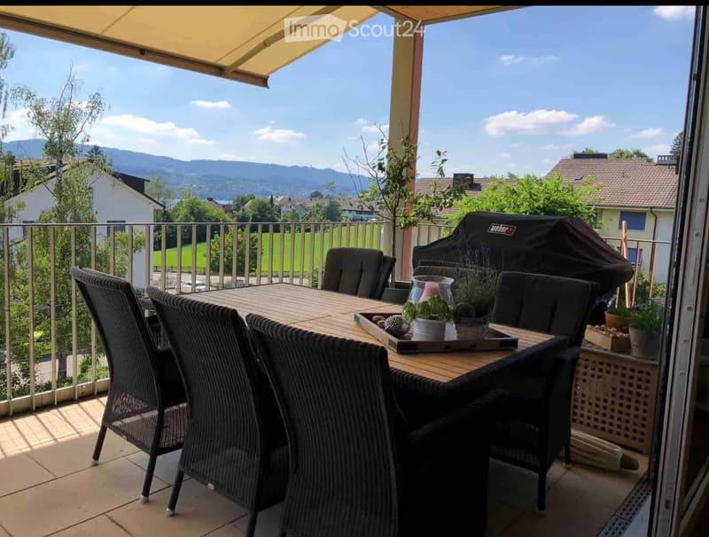Balcony with outdoor dining set, grill, potted plants, and scenic mountain view.
