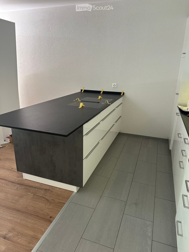 Empty kitchen area with a black countertop, white cabinets, and grey tiled floor. No furniture or appliances are present.