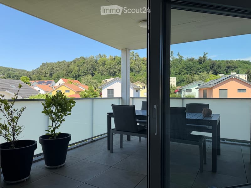 Balcony with a dining set including a table and chairs, two potted plants, and a scenic view of houses and greenery.